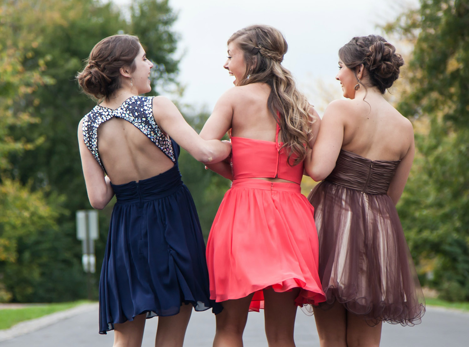 Friends locking arms laughing in prom dresses